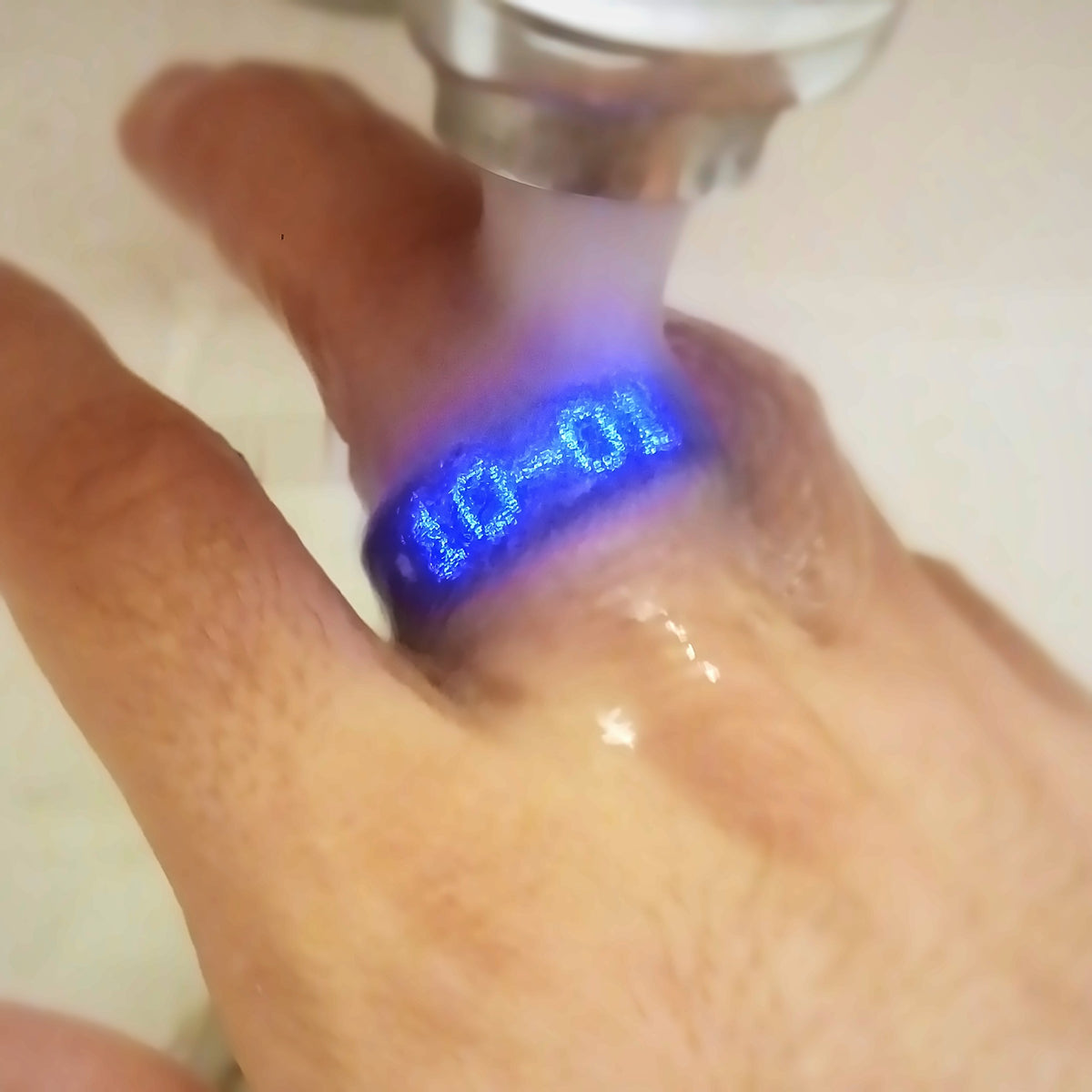 Bague connectée allumée sous l'eau du robinet, l'écran affiche la date
